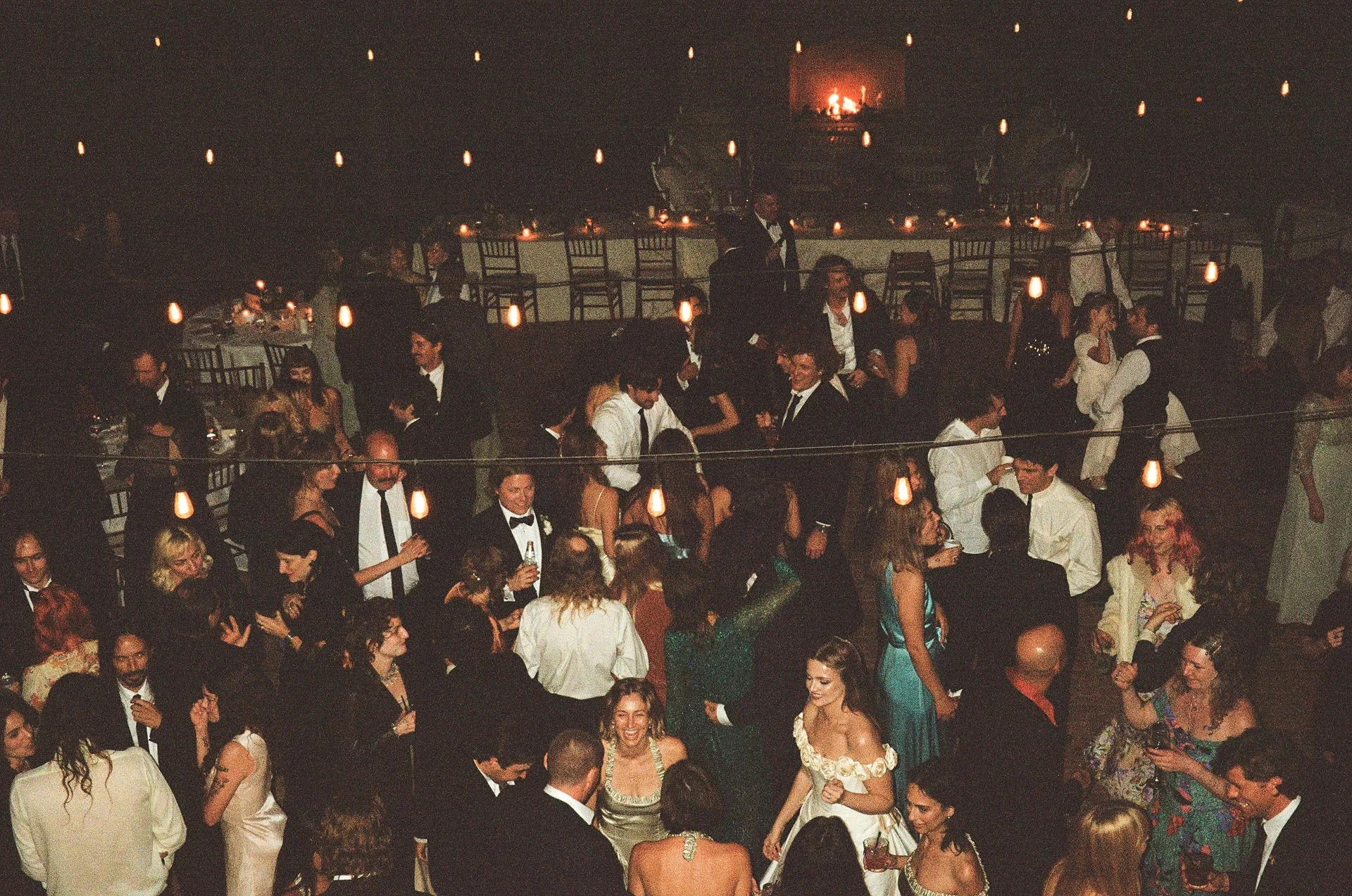 Guests packed shoulder to shoulder outdoors at night under strings of warm bulbs