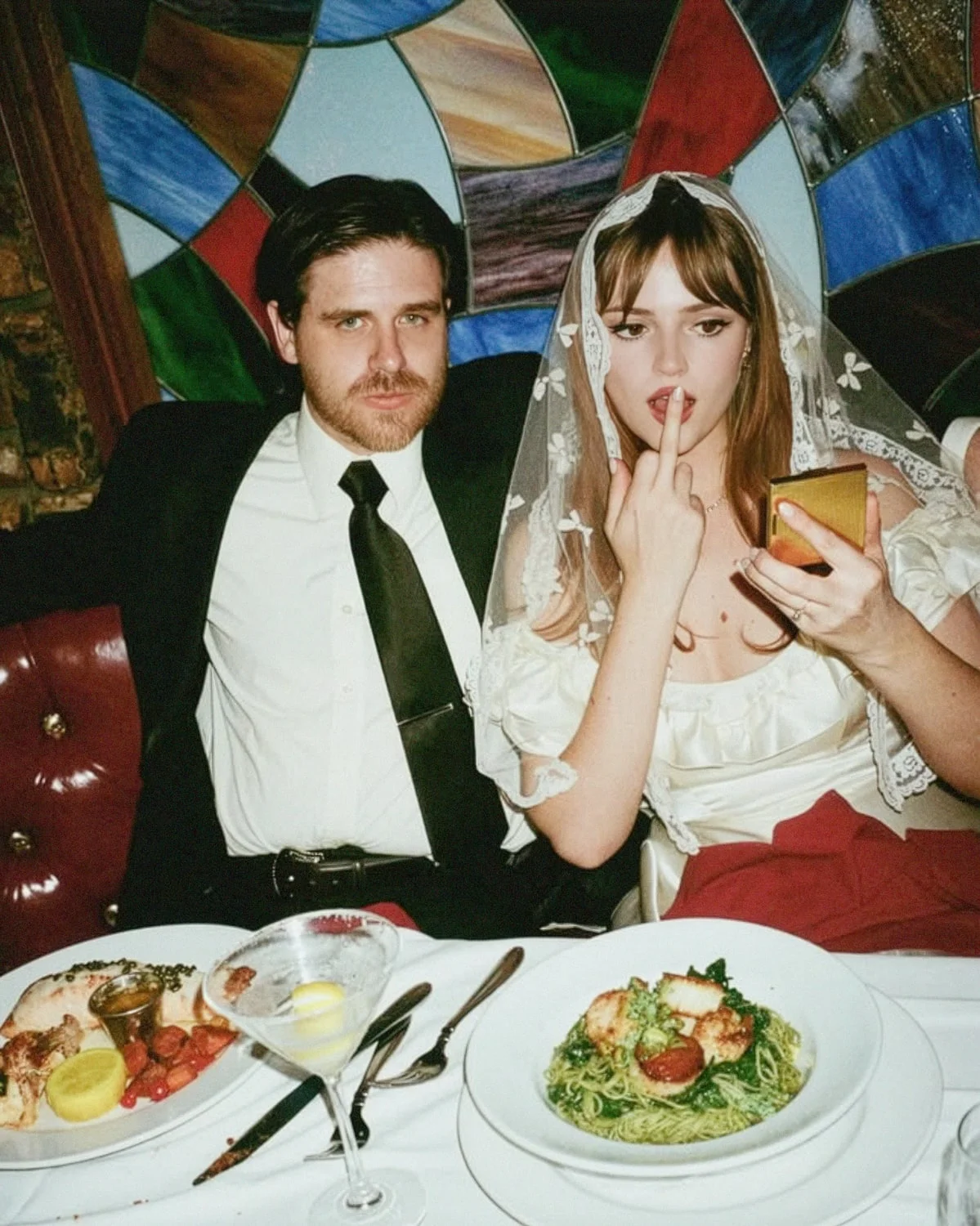 Couple in a restaurant booth against stained glass, dinner on the table